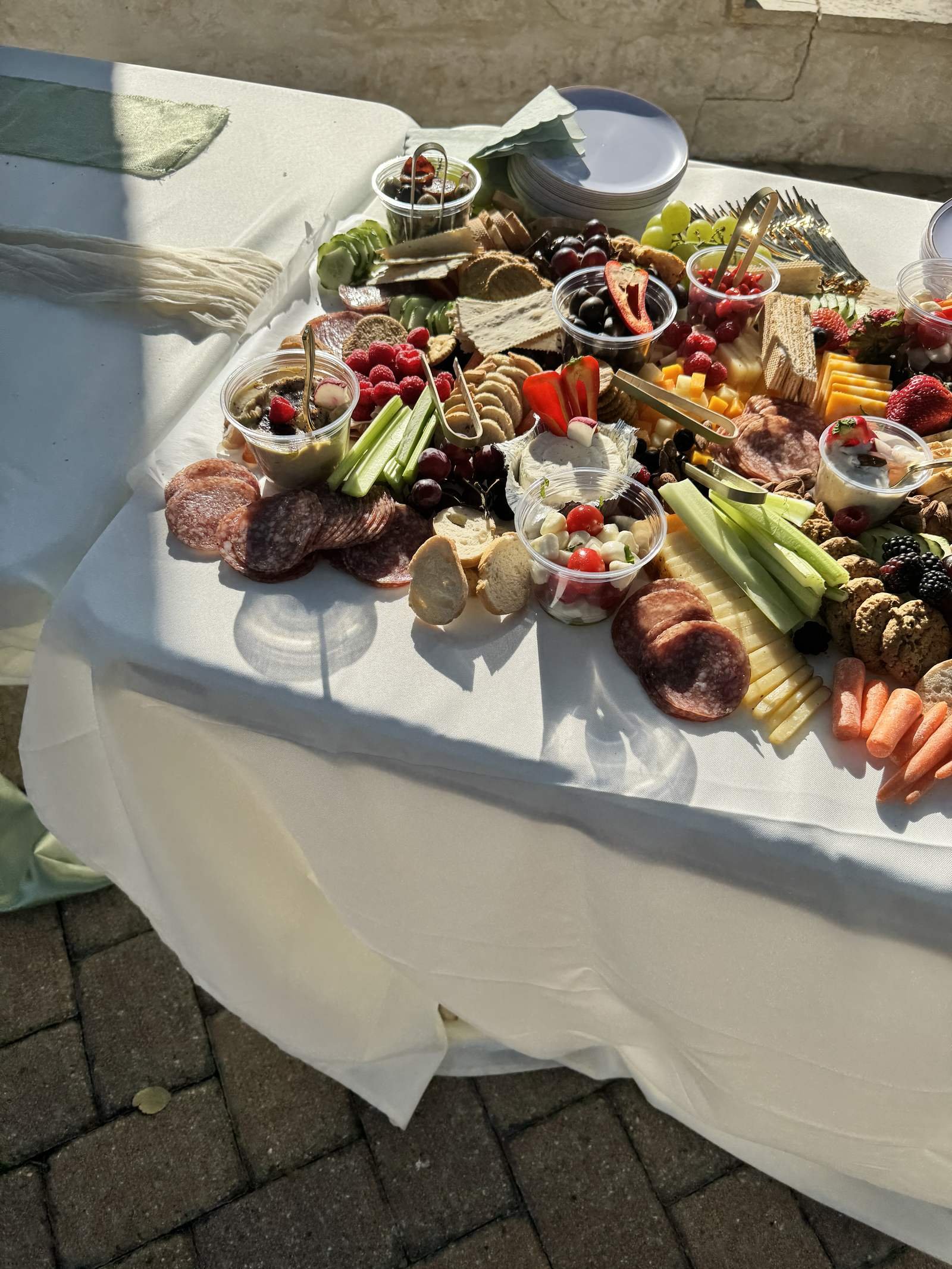 Close-up of a charcuterie spread with cured meats, berries, celery, carrots, and small bowls of dips on a white tablecloth