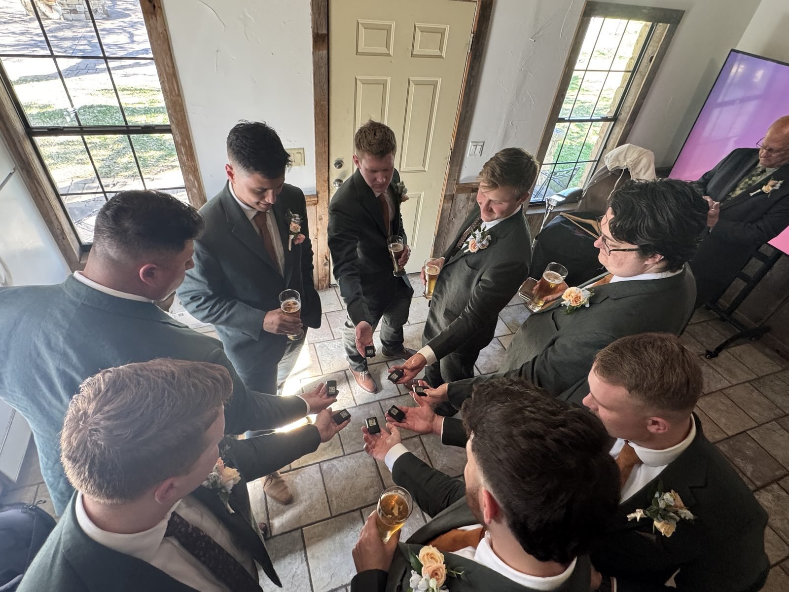 Groomsmen in matching dark green suits gathered in a circle holding small gift boxes while getting ready